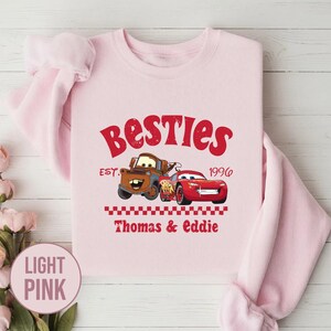 May include: Light pink sweatshirt with the word "Besties" in red script. The design includes cartoon images of two cars, a brown truck and a red race car, with the text "Thomas & Eddie" below.