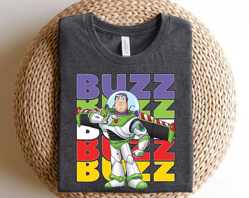 Puede incluir: Camiseta gris oscuro con un gr&aacute;fico de Buzz Lightyear de Toy Story. El dise&ntilde;o incluye la palabra "BUZZ" en letras apiladas y coloridas. Buzz est&aacute; representado con su traje espacial verde y blanco.