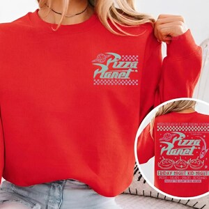 May include: A red sweatshirt featuring the Pizza Planet logo in teal and white. The design includes the text "Pizza Planet" with a checkerboard pattern. The back of the sweatshirt has additional text and graphics.