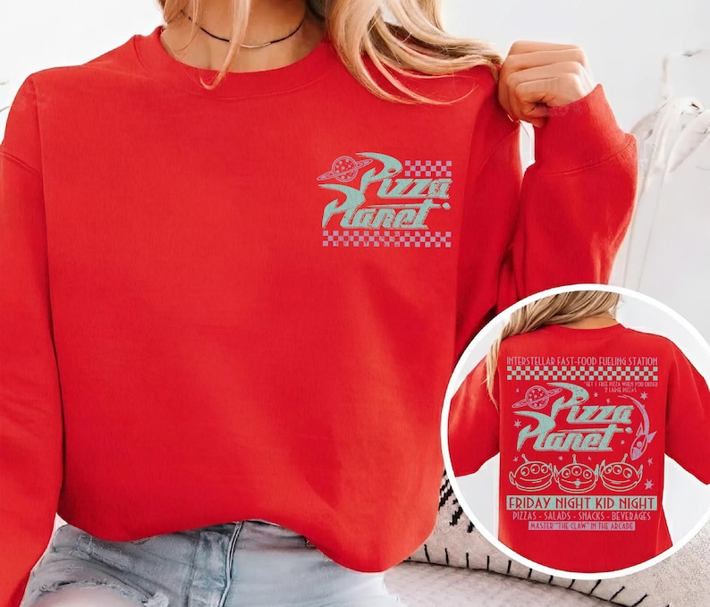 May include: A red sweatshirt featuring the Pizza Planet logo in teal and white. The design includes the text "Pizza Planet" with a checkerboard pattern. The back of the sweatshirt has additional text and graphics.