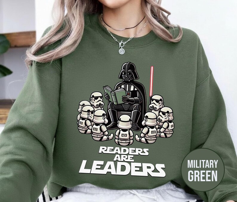 K&ouml;nnte beinhalten: Milit&auml;rgr&uuml;nes Sweatshirt mit einer Grafik von Darth Vader, der Stormtroopern vorliest. Der Text "Readers are Leaders" befindet sich darunter. Ein rotes Lichtschwert ist sichtbar. Das Sweatshirt ist einfarbig.