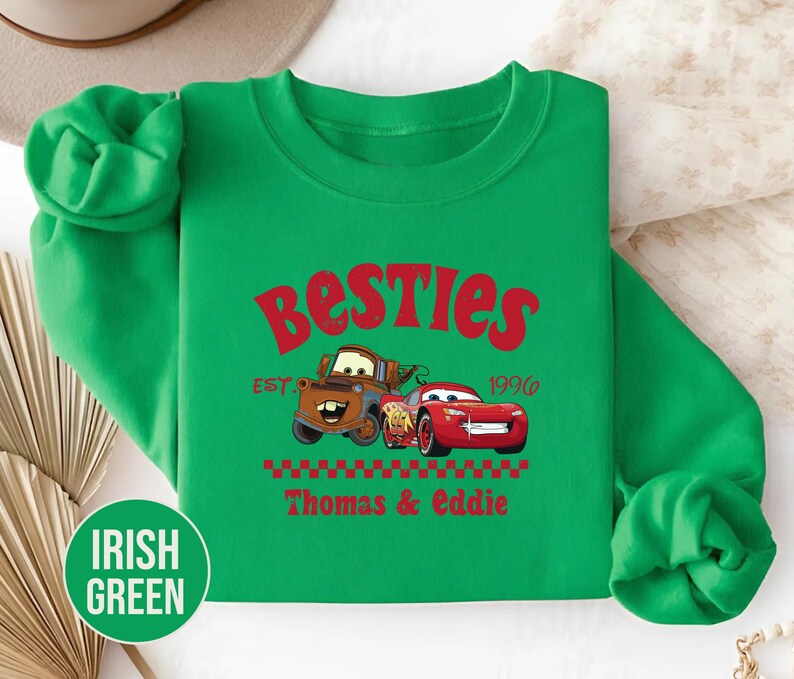 May include: Irish green sweatshirt featuring the text "Besties" in red, along with the year "1996". The design includes cartoon images of two cars, with the names "Thomas & Eddie" below. The sweatshirt has a crew neck and long sleeves.