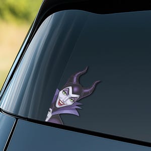 K&ouml;nnte beinhalten: Ein Autoaufkleber mit Maleficent, der Disney-B&ouml;sewichtin, mit ihren ikonischen H&ouml;rnern, gr&uuml;nen Augen und lila Kragen. Der Aufkleber ist f&uuml;r die Anbringung an einer Autoscheibe konzipiert.