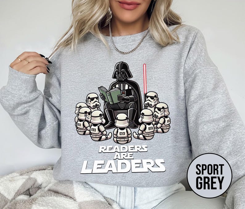 K&ouml;nnte beinhalten: Sportgraues Sweatshirt mit einer Grafik von Darth Vader, der Stormtroopern vorliest. Der Text "Readers are Leaders" steht unter der Grafik. Ein rotes Lichtschwert ist sichtbar. Das Sweatshirt hat lange &Auml;rmel.