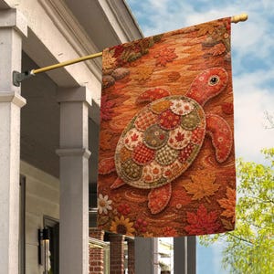 May include: A rectangular garden flag featuring a turtle with a shell made of various patterned fabric circles in shades of orange, green, and white. The background displays a textured autumn scene with fallen maple leaves and flowers.