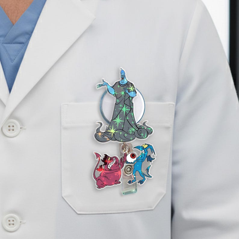 May include: A retractable badge reel with cartoon character designs. The top character is a blue figure in a dark grey robe with green stars. Below are two smaller characters, one red and one blue, with a red eyeball in the middle.
