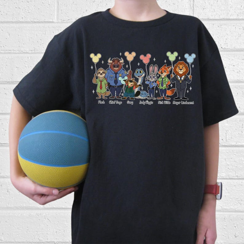 May include: Black t-shirt featuring a colorful graphic of characters from the movie Zootopia, each holding a Mickey Mouse-shaped balloon. The characters include Flash, Chief Bogo, and Judy Hopps. The names of the characters are printed below them.