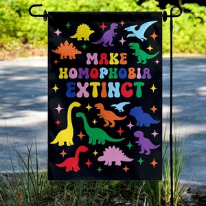 May include: Black garden flag with colorful dinosaur illustrations and the text "MAKE HOMOPHOBIA EXTINCT." The flag features a variety of dinosaurs in shades of yellow, orange, green, purple, and blue, along with star accents.