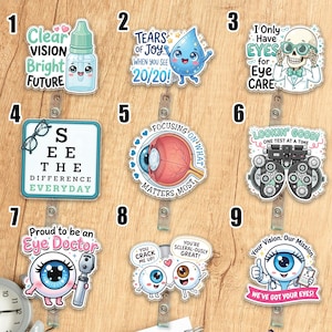 May include: A collection of nine acrylic badge reels featuring eye-themed illustrations and text. Designs include a smiling eye drop, a skeleton wearing glasses, an eye chart, a human eye, a phoropter, and cartoon eyes with puns about vision care.