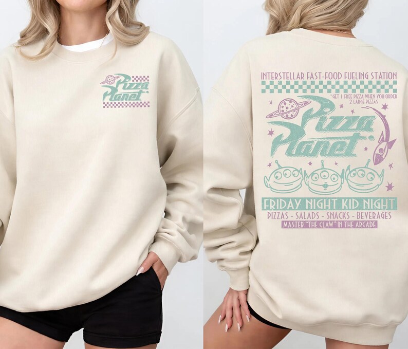 May include: Beige sweatshirt with the Pizza Planet logo on the front and back. The back features the text "INTERSTELLAR FAST-FOOD FUELING STATION" and "FRIDAY NIGHT KID NIGHT" with alien graphics and other text.