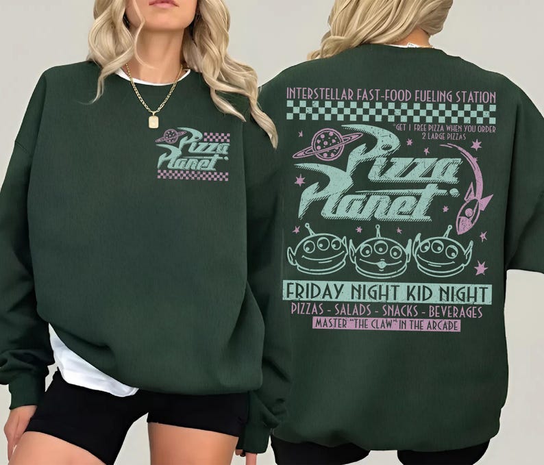 May include: Dark green sweatshirt with the Pizza Planet logo on the front and back. The back features the text "INTERSTELLAR FAST-FOOD FUELING STATION" and "FRIDAY NIGHT KID NIGHT". The design includes alien characters and a space theme.