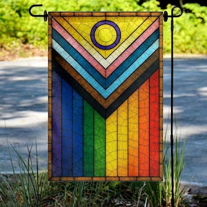 May include: A stained-glass style garden flag featuring a vibrant design. The flag showcases a rainbow of colors, including red, orange, yellow, green, blue, and purple, with a yellow circle and a chevron pattern. The flag is displayed on a black metal stand.