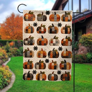 May include: A rectangular garden flag featuring a repeating pattern of patchwork-style pumpkins in shades of orange, black, brown, and cream. The pumpkins are arranged in rows against a textured cream background, interspersed with small black stars.