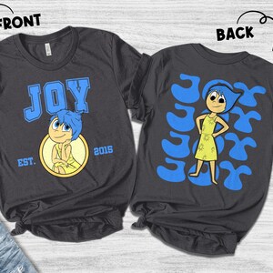 May include: Dark gray t-shirts featuring the character Joy from the movie Inside Out. The front of the shirt has the word "JOY" in blue block letters, the character Joy, and the text "EST. 2015". The back of the shirt has a graphic of Joy.