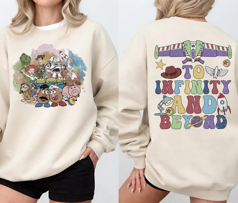 May include: Cream-colored sweatshirt featuring a colorful graphic of Toy Story characters on the front. The back of the sweatshirt has the phrase "TO INFINITY AND BEYOND" with various themed illustrations. A comfortable, casual style.