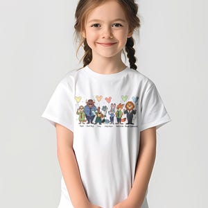 May include: White t-shirt featuring a colorful graphic of characters from the movie Zootopia, including Flash, Chief Bogo, Gary, Judy Hopps, Nick Wilde, and Mayor Lionheart. The characters are arranged in a row with balloons above them. The names of the characters are printed below.