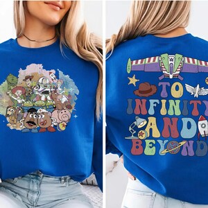May include: Royal blue sweatshirt featuring a colorful graphic of Toy Story characters on the front. The back of the sweatshirt displays a Buzz Lightyear design with the phrase "To Infinity and Beyond" in a retro font.