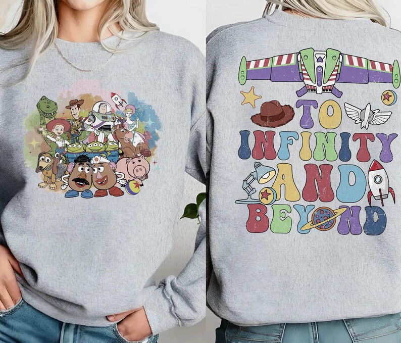 May include: A light gray sweatshirt featuring a colorful graphic of characters from a popular animated film on the front. The back of the sweatshirt has the phrase "TO INFINITY AND BEYOND" with related imagery. The design includes a rocket, a star, and a space ship.
