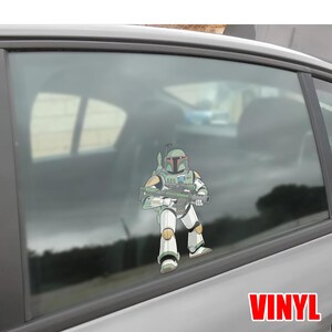 Puede incluir: Una calcoman&iacute;a de vinilo de Boba Fett de Star Wars, sosteniendo un rifle bl&aacute;ster. El personaje est&aacute; representado con su armadura verde, blanca y amarilla. La palabra "VINYL" est&aacute; impresa en rojo en la parte inferior derecha.