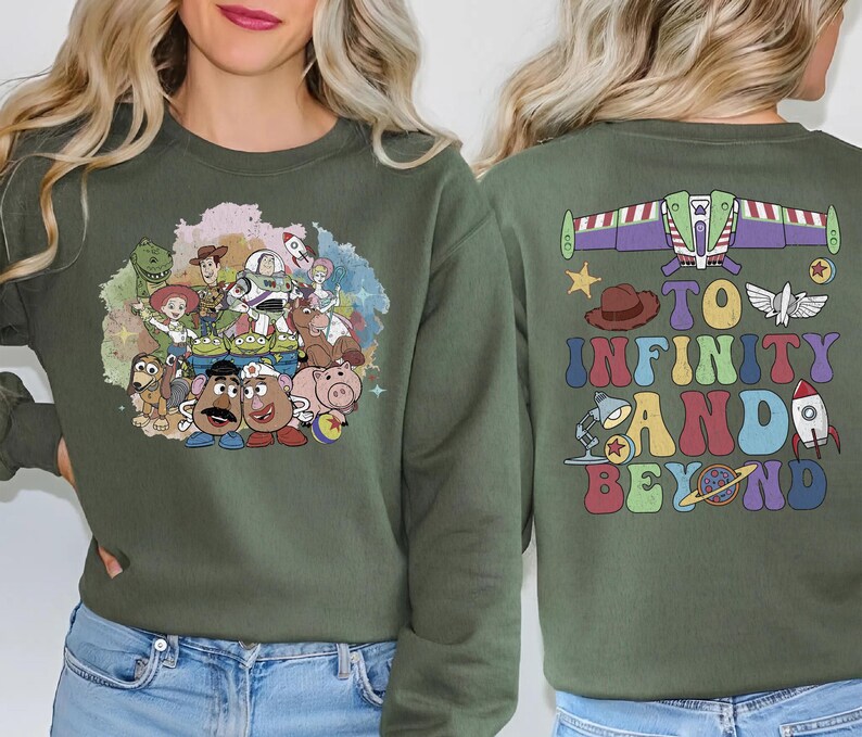 May include: Olive green sweatshirt featuring a colorful graphic of Toy Story characters on the front. The back of the sweatshirt displays Buzz Lightyear's spaceship and the phrase "To Infinity and Beyond" in a retro font.