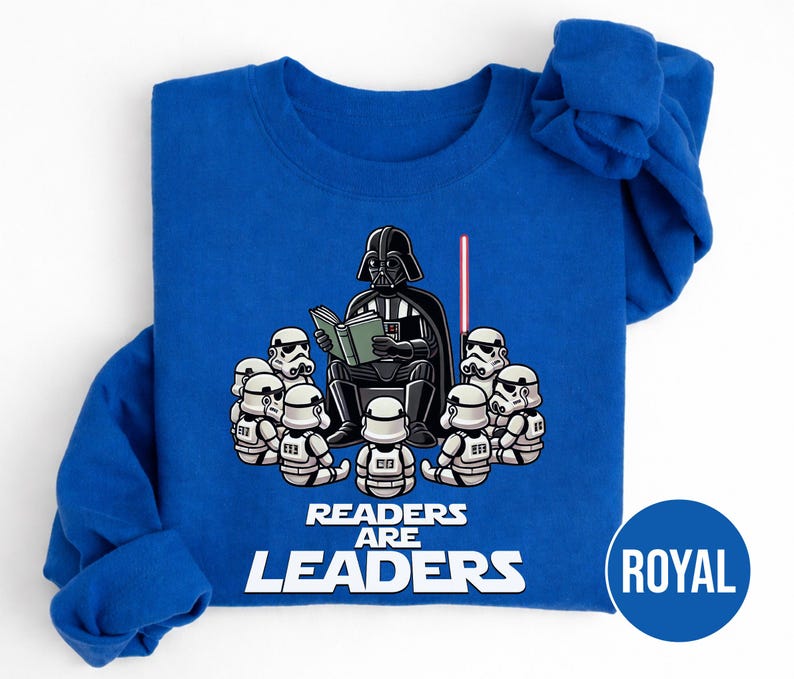 K&ouml;nnte beinhalten: K&ouml;nigsblaues Sweatshirt mit einer Grafik von Darth Vader, der Stormtroopern vorliest. Der Text "Readers are Leaders" ist unter der Illustration aufgedruckt. Ein rotes Lichtschwert ist ebenfalls zu sehen.
