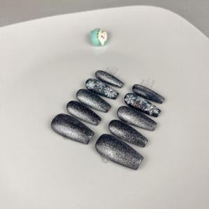 May include: Set of ten silver glitter coffin-shaped press-on nails with snowflake designs.