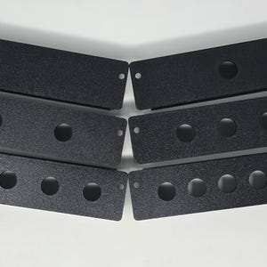May include: Six black rectangular metal panels with a textured finish, arranged in two columns. Each panel features small circular holes at the ends and varying numbers of larger circular cutouts along the center, ranging from zero to five holes.