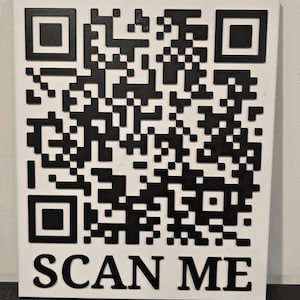 Könnte beinhalten: Ein weißes quadratisches Schild mit einem schwarzen QR-Code und dem Text "SCAN ME" in schwarzen Buchstaben. Der QR-Code ist ein komplexes Muster aus schwarzen und weißen Quadraten. Für schnellen Informationszugriff.