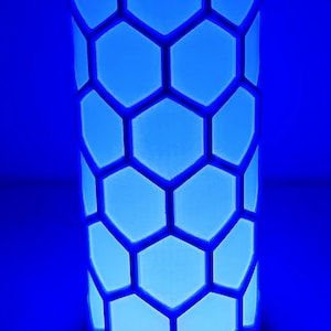 May include: A white cylindrical lamp with a honeycomb pattern. The lamp is illuminated with a bright blue light.