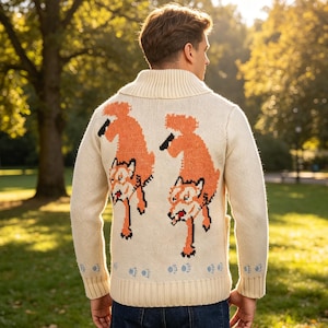 May include: A cream-coloured knitted sweater with a shawl collar and cuffs. The back displays two orange fox designs with black details. The person is in a park, with trees and sunlight visible in the background.