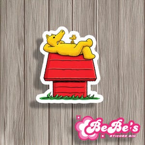 May include: A sticker featuring a yellow cartoon bear relaxing on a red doghouse with a small yellow bird. The doghouse has a white outline and sits on green grass. The sticker has a white border.