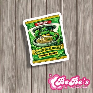 May include: A sticker featuring a green turtle character eating ramen from a sewer. The sticker is designed to look like a ramen packet, with the words "RAMEN!" and "SEWER SHELL NINJAS MUTANT FLAVOR" printed on it. The background is a wooden surface.