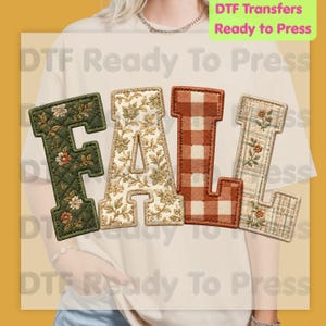 May include: A beige t-shirt featuring the word FALL in large block letters. The F is dark green with a floral pattern, the A is cream with a floral print, the L is orange and white gingham, and the second L is a plaid pattern with flowers.