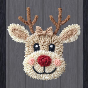 May include: A handmade reindeer face made of yarn. The reindeer has brown antlers, a red nose, black eyes, and pink cheeks. A small bow sits between the antlers. The background is a dark wood grain.