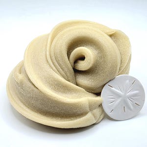 Puede incluir: Una sustancia beige claro, arremolinada, parecida a la masilla, con un objeto blanco en forma de estrella. La masilla tiene forma de espiral, y el objeto blanco tiene un dise&ntilde;o de estrella con l&iacute;neas que irradian desde el centro.