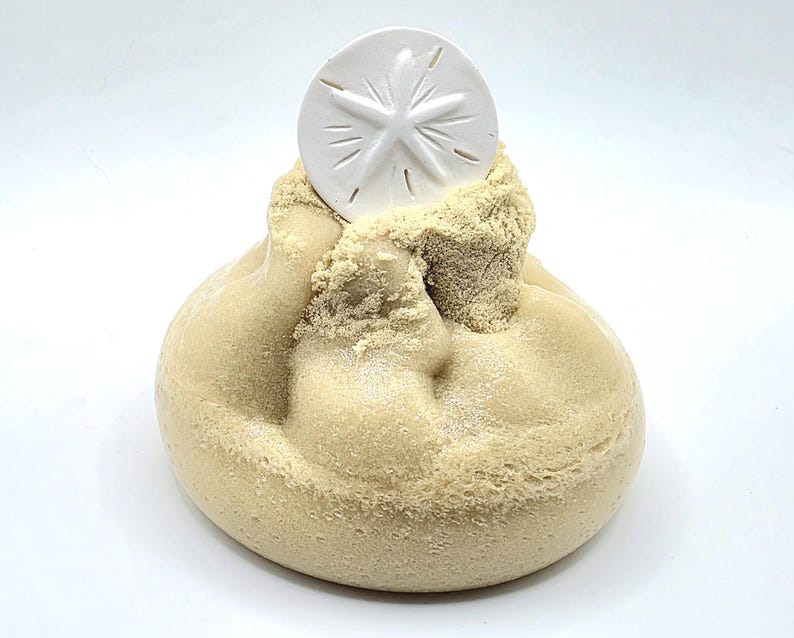 Puede incluir: Una escultura beige y redondeada con una textura similar a la arena, coronada por un d&oacute;lar de arena blanco. El d&oacute;lar de arena tiene un dise&ntilde;o en forma de estrella. La escultura evoca un tema de playa y decoraci&oacute;n costera.