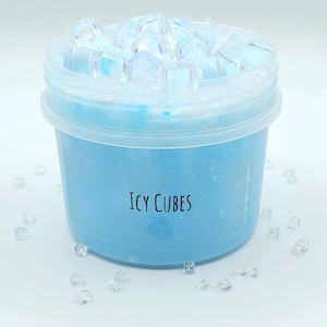 May include: A clear plastic container filled with light blue slime and topped with clear, cube-shaped decorations. The text "Icy Cubes" is printed on the container. Scattered clear cubes are around the container.