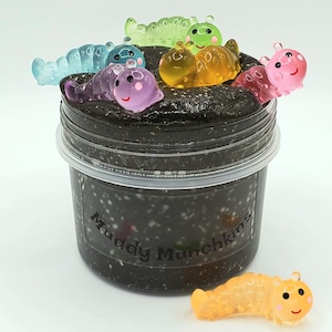 May include: A black slime with glitter in a clear jar with a label that says "Muddy Munchkins".  The slime is topped with colorful plastic worm toys.