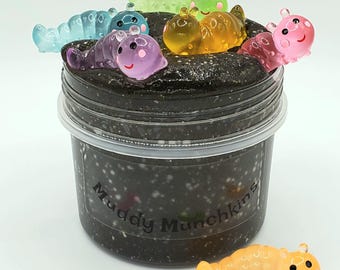 May include: A black slime with glitter in a clear jar with a label that says "Muddy Munchkins".  The slime is topped with colorful plastic worm toys.