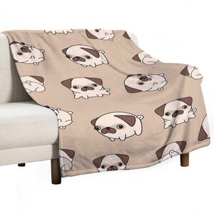 May include: A beige throw blanket featuring a repeating pattern of cartoon pugs in various poses. The pugs are white with brown markings and black outlines. The blanket is draped over a beige sofa.
