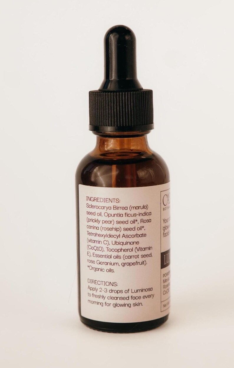 May include: A brown glass bottle with a black dropper top. The label lists ingredients like marula seed oil and rosehip seed oil. The text on the label says to apply 2-3 drops of Luminosa to the face for glowing skin.