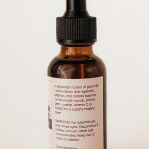 May include: A brown glass bottle with a black dropper top. The label includes text about plant oils, antioxidants, and ingredients like marula and vitamin C. The bottle is for external use only.