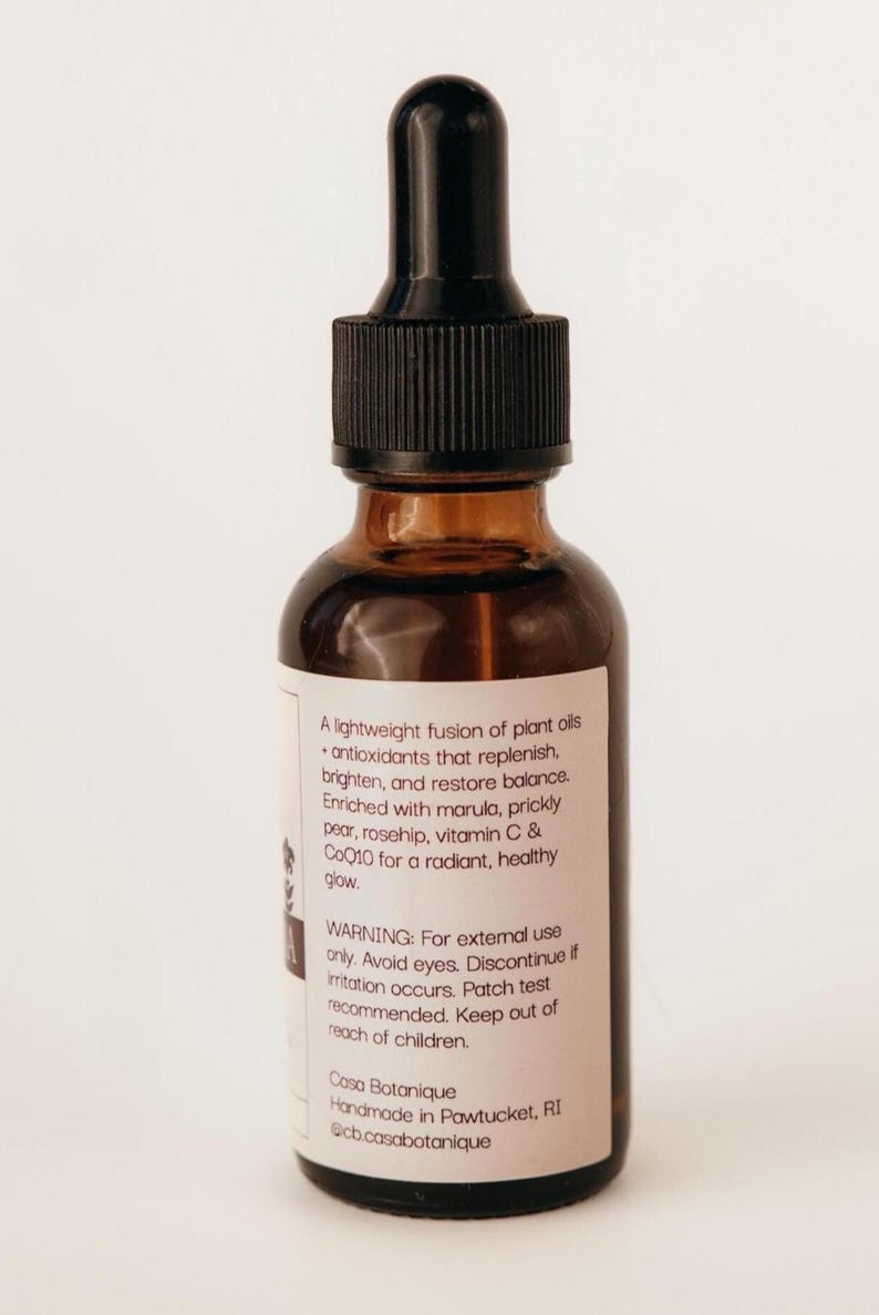 May include: A brown glass bottle with a black dropper top. The label includes text about plant oils, antioxidants, and ingredients like marula and vitamin C. The bottle is for external use only.