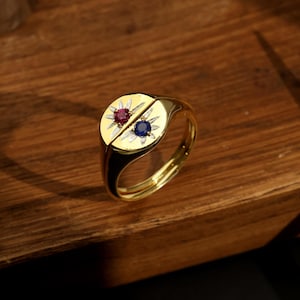 May include: A gold signet ring featuring a red and blue gemstone set in a starburst design.