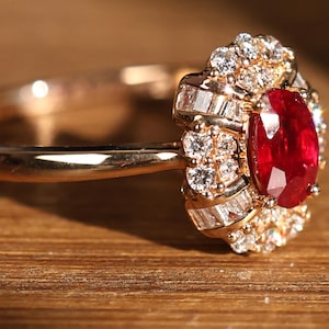 Könnte beinhalten: Ein goldener Ring mit einem großen roten Rubin-Edelstein, der von kleineren Diamanten umgeben ist. Der Ring ist in einem floralen Design gefasst.