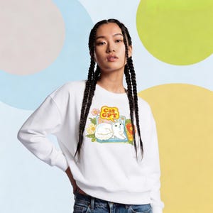 May include: White sweatshirt with a graphic of a white cat and the text "Cat GPT". The cat is in a floral setting. The sweatshirt is a long-sleeved crew neck. The design has a retro style.