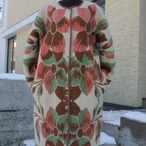May include: A long, cream-colored coat with a floral pattern in shades of pink, green, and brown. The coat has a button closure and a collar.