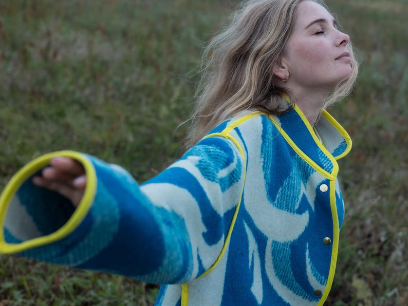 May include: A blue and white patterned jacket with yellow trim. The jacket has a button-up front and a unique wave-like design. The sleeves are long and the collar is yellow.