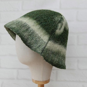 Peut inclure: Un chapeau en feutre vert et blanc avec un bord. Le chapeau est présenté sur une tête de mannequin contre un mur de briques blanches. Le chapeau a un aspect texturé avec un dégradé de rayures vertes et blanches.