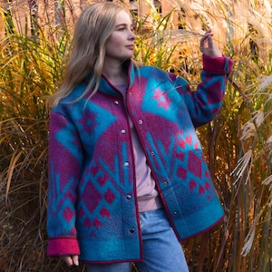 May include: A turquoise and magenta patterned jacket with a button-up front. The jacket features a geometric design and magenta trim. The person is wearing blue jeans and a pink shirt.